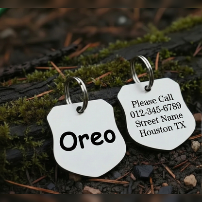 Two silver pet tags with engraved text on a natural background